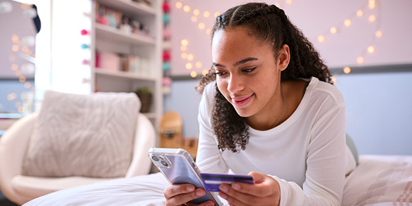 teen girl laying on bed holding phone and debit card