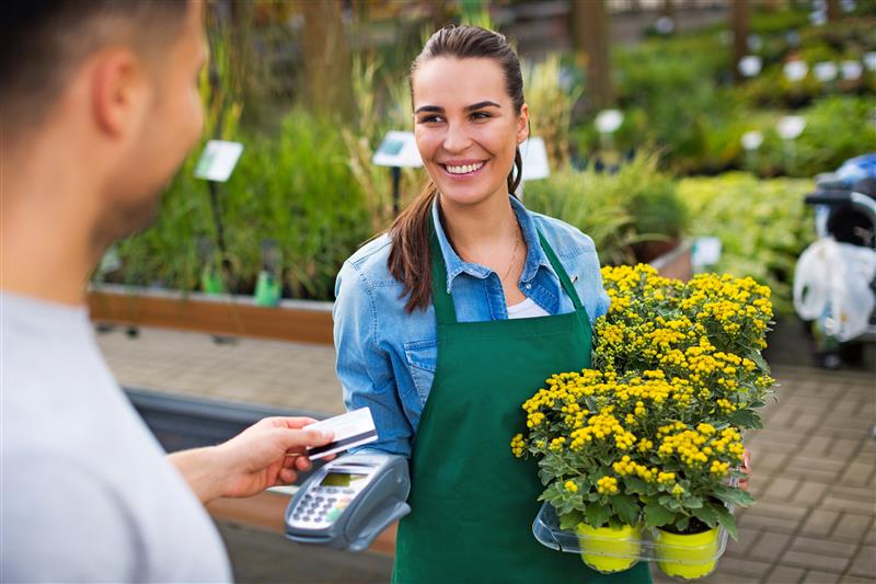 A man uses a contactless card to purchase flowers from a woman. 