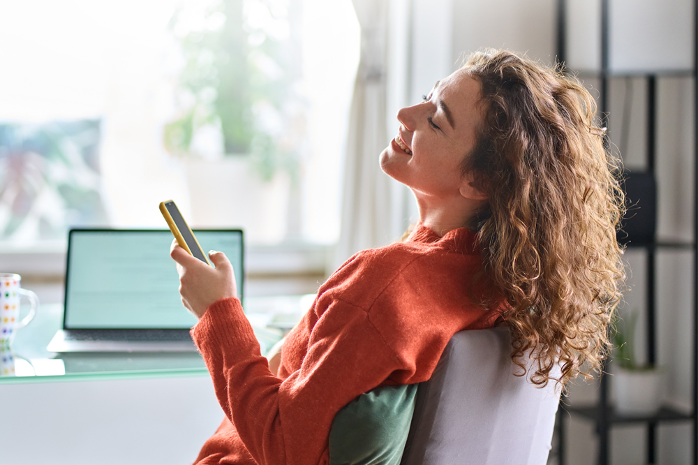 relaxed woman smiling while holding phone with eyes closed