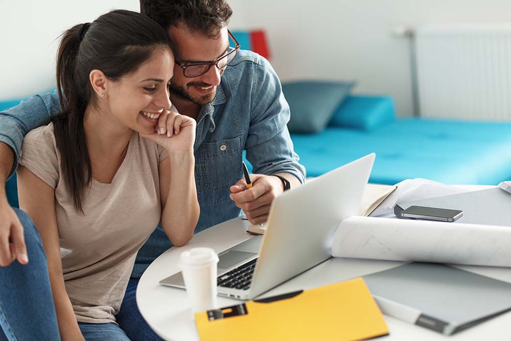 couple happily looking at laptop together with papers around them