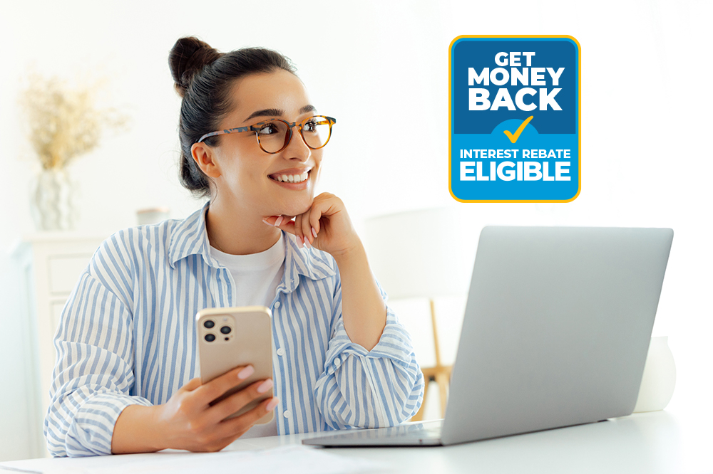 Woman in glasses holding a phone in front of a laptop with the words "Get Money Back- Interest Rebate Eligible" in a rectangle