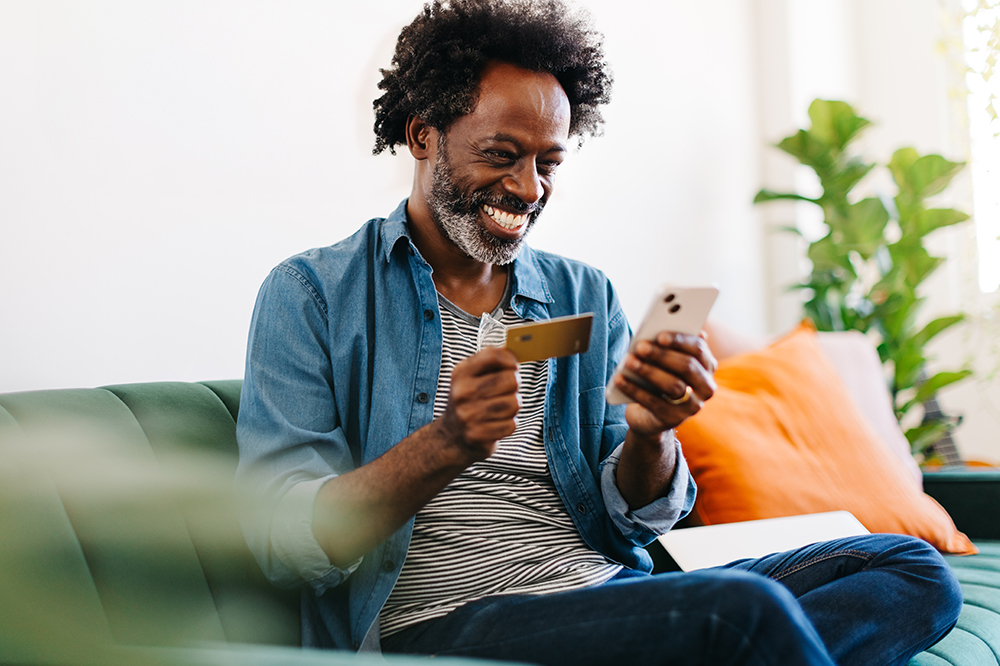 A man smiles at his smartphone while holding a credit card. 