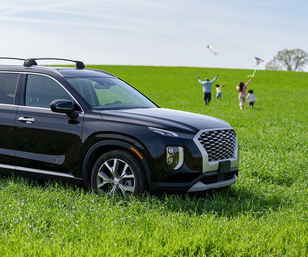 Closeup of an SUV in the grass with a family flying kites in the background