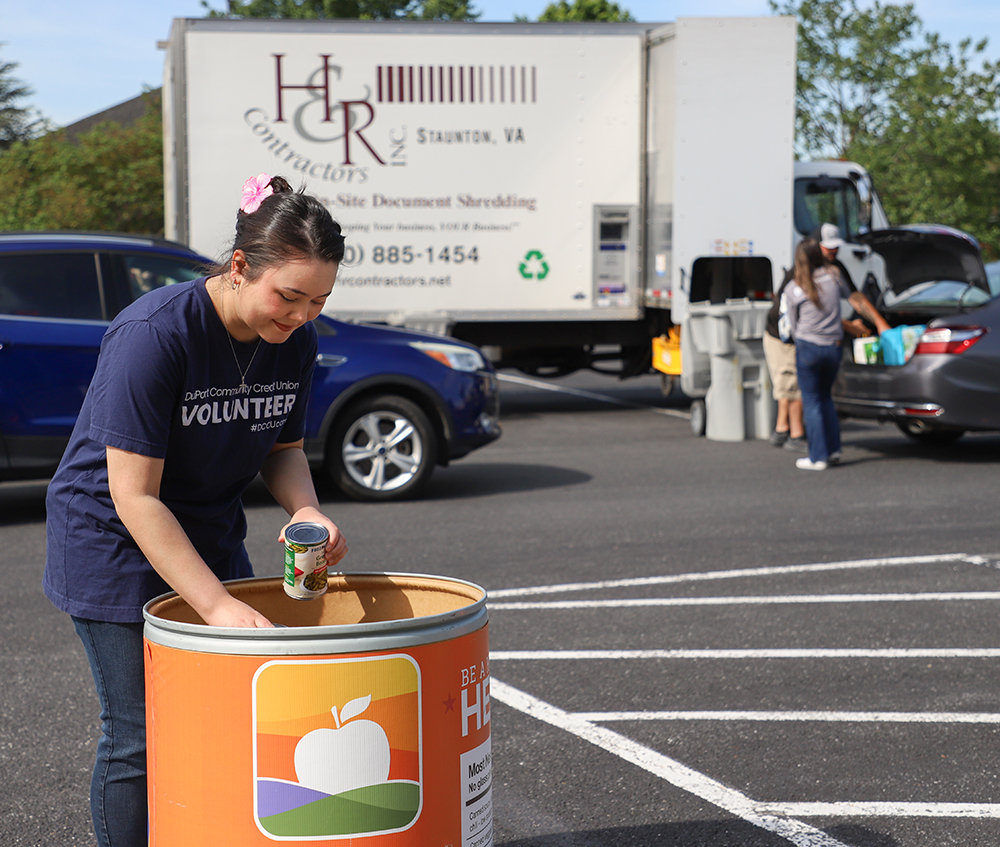 Woman placing canned goods into a donation container in front of a shred truck